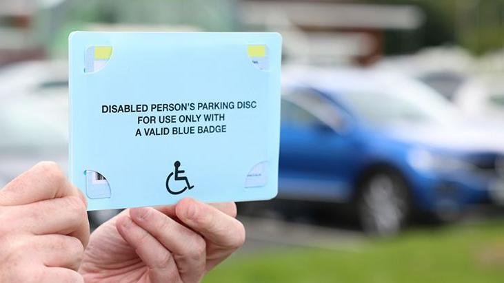 A person holding up the reverse side of a Blue Badge parking disc