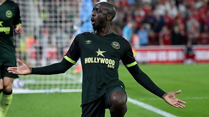 Yoane Wissa celebrates scoring for Brentford with one knee on the ground and his arms outstretched