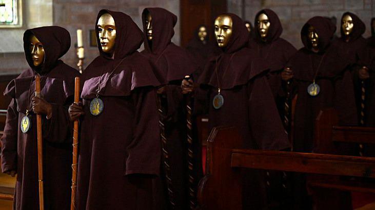 A procession of cloaked traitors wearing gold masks