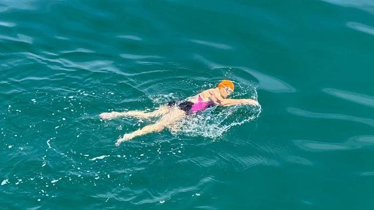 Dot, who wears an orange swimming cap and goggles, swims in the channel.