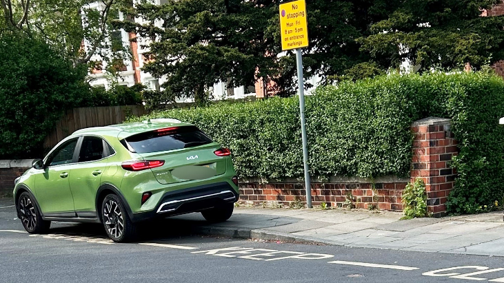 Green car parked over road markings saying 'school keep clear'