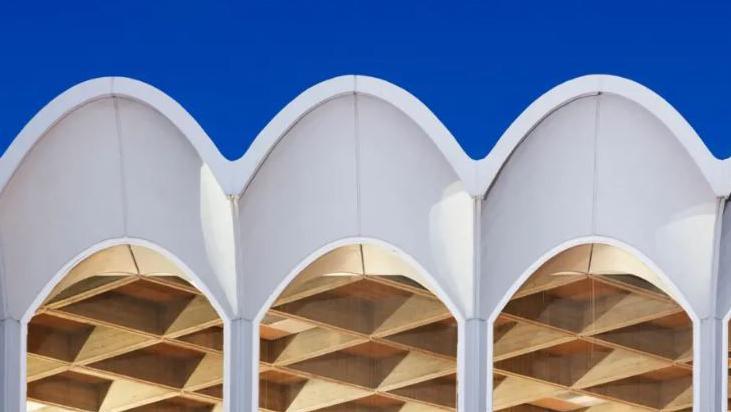 A 1960s white framed arched roof line above arched windows - and set against a blue sky - at Fitzwilliam College, Cambridge.