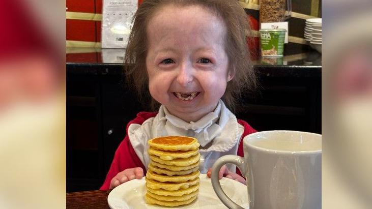 An image of Isla smiling with a large stack of pancakes on her plate