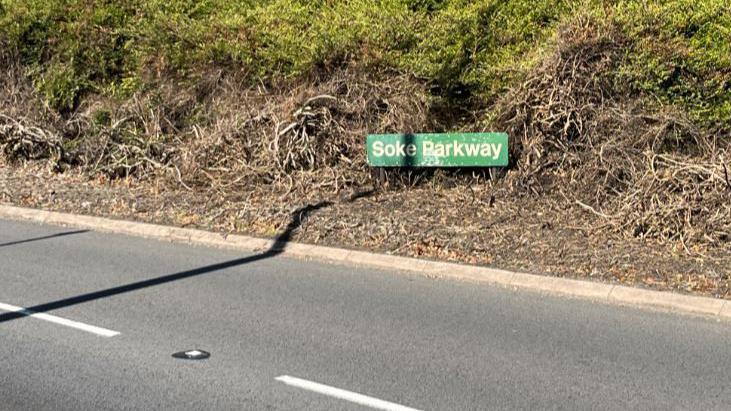 A lay-by road with a green Soke Parkway signboard placed on bushes next to the slip road.