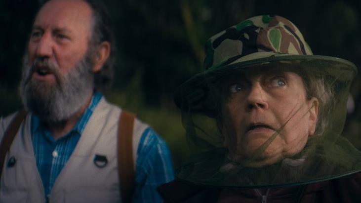 A still from the teaser showing a man and a woman. The woman is wearing a hat and netting to protect her from biting midges.