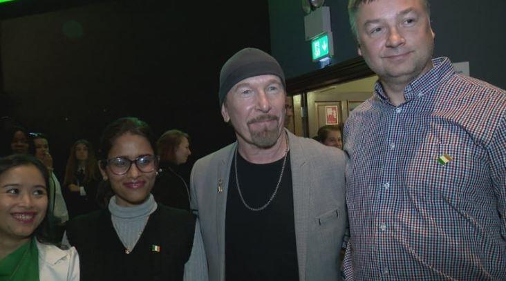 David Howell Evans, with beard and grey hat, grey jacket and necklace, third from the left. He is accompanied on his left, by a woman with dark hair, green top and white jacket, a woman with dark hair, black top and grey jumper and a man with grey hair and red/blue striped shirt.