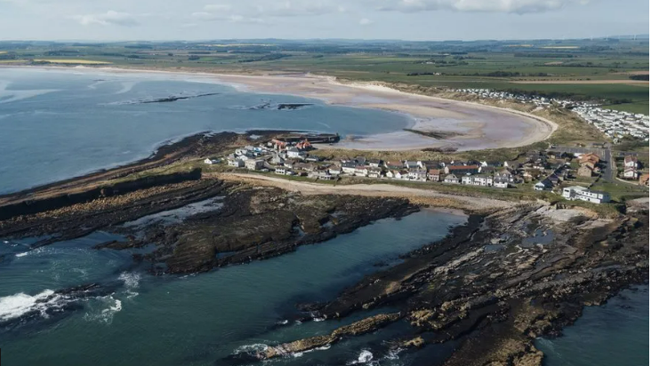 An aerial view of Beadnell showing a row of houses along the cliff and the sweep of the bay behind 