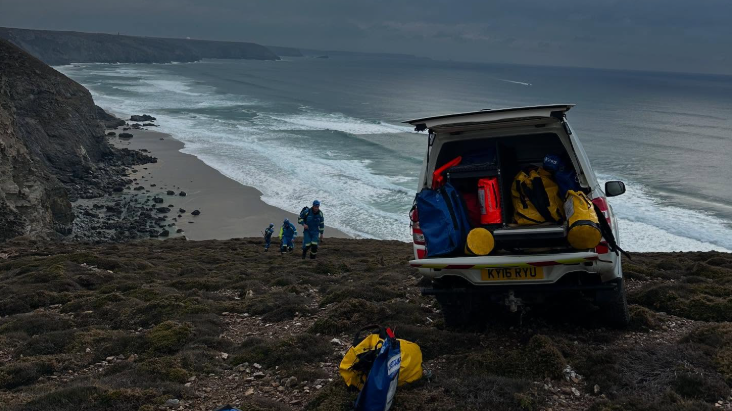 A coastguard van with equipment visible on a cliff with three people approaching.