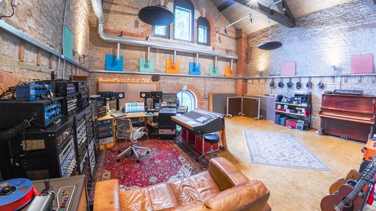 The inside of the recording studio in a brick-lined spacious room with various instruments, including a piano, keyboard and guitars and and sizable recording equipment