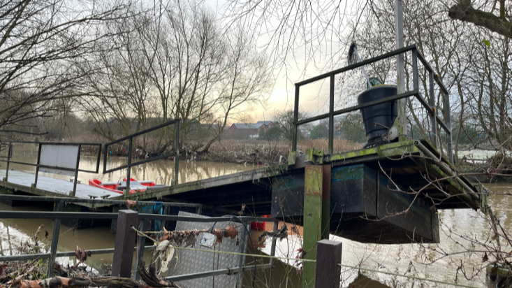 A pontoon dock, by a river, which has been lifted up into the air by rising water 