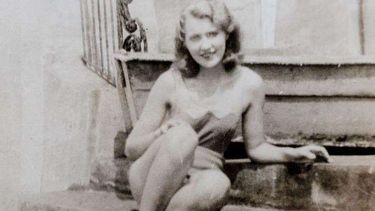 A sepia image of Mary An MacLeod from 1932. She is 20 years old and lounging on the steps of a house. 