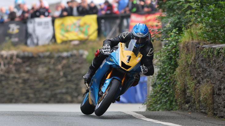 Daniel Ingham on the race track one a blue and yellow bike with a yellow plate with the number one on it. He's wearing black leathers and a blue helmet.