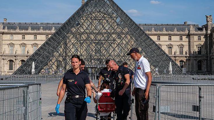 Firefighters from the Paris Fire Brigade escort a person outside the Louvre Museum during an intense heatwave on 25 June 2026