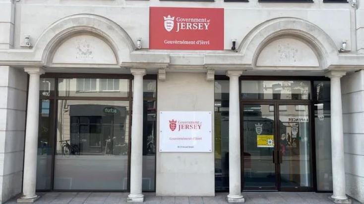 Government of Jersey building with large windows set behind four stone pillars with two 'government of Jersey' signs on the building