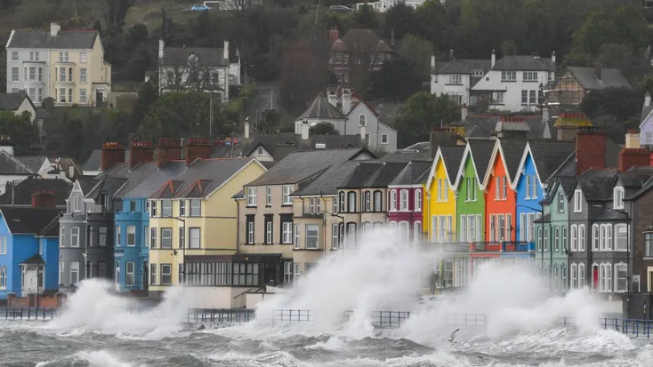 A row of colourful terraced houses on the coastline are sprayed by waves which are crashing onto the streets.