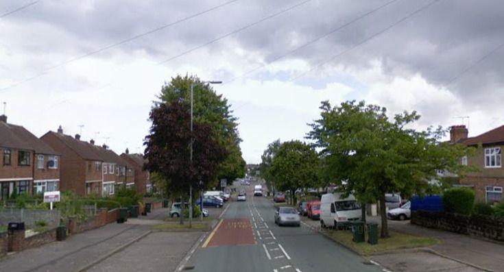 Clifford Bridge Road as shown on Google Street View. The road has houses on either side and some large trees and parked cars and a white van also parked. There are road markings down the centre of the street. 