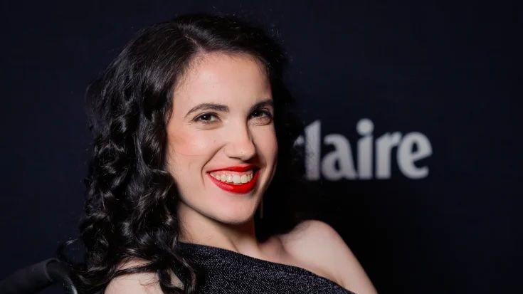 A woman with black hair, red lipstick and a black dress smiling