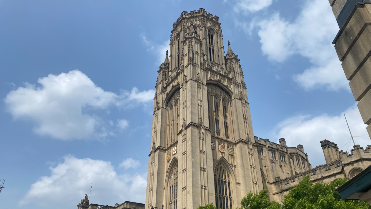 A shot of the Wills Memorial Building from the top of Park Street, the sandstone coloured gothic tower is backdropped by a blue sky