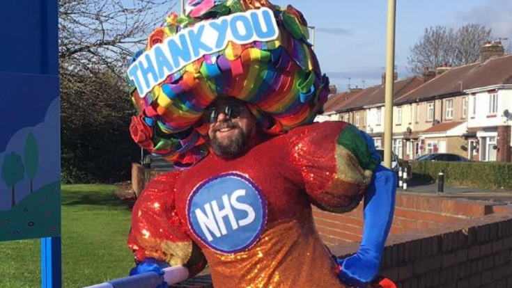 Colin wearing a huge dress with NHS on it - and a headdress which says Thank you