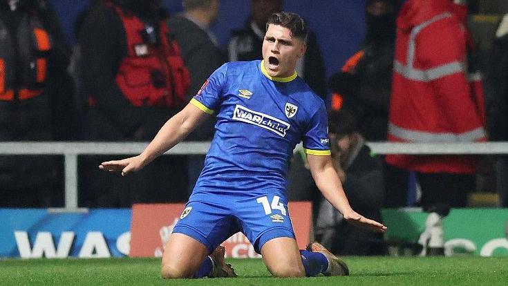 Matt Stevens slides on his knees to celebrate a goal for AFC Wimbledon