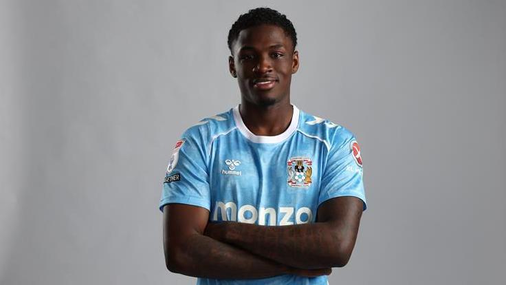 Jahnoah Markelo poses with arms crossed in a sky blue Coventry City shirt after signing for the club