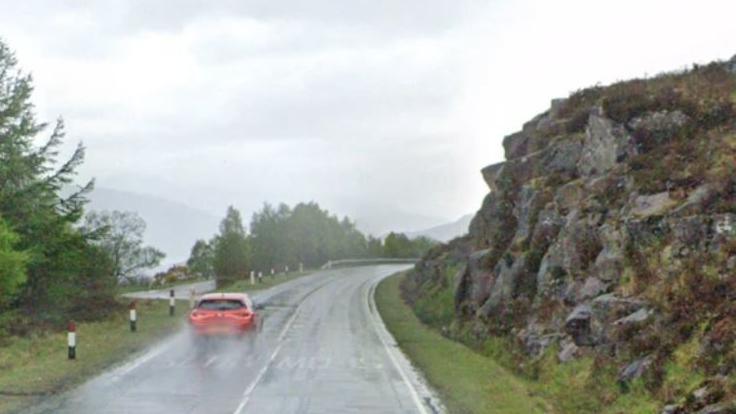 Carbad dearg a' dràibheadh air an A87 faisg air Cluanaidh agus an t-uisge ann.