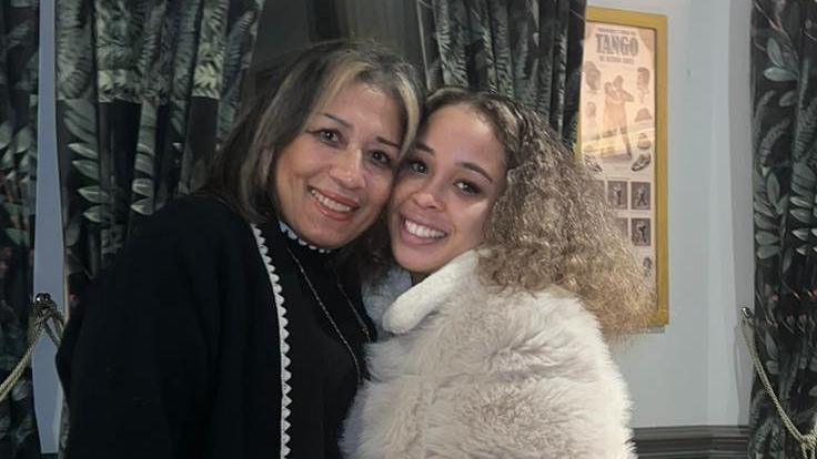 Two women smiling into camera. One woman is wearing a black outfit and another woman is wearing a fluffy white coat. 