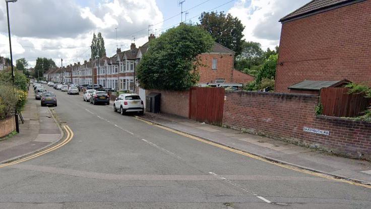 A Google street view showing a road of terraced houses with gable windows and cars parked outside. The Dartmouth Road street sign can be seen on a low wall to the right.