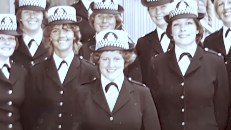 A black and white photo of eight female police officers in smart uniform. They are all smiling and standing shoulder to shoulder.