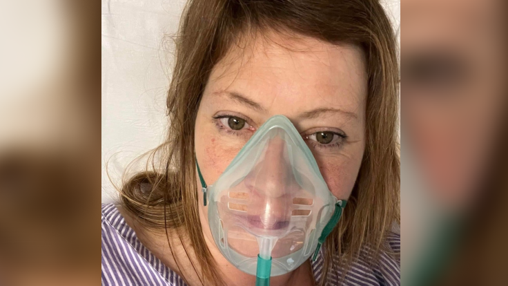 Kerry Fear, wearing a clear mask which helps her breathe. She is dressed in a blue and white striped top and has shoulder length brown hair.