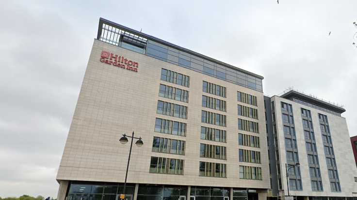 The exterior of a nine-storey building with a lamp post in front of it, and a sign that reads "Hilton Garden Inn"