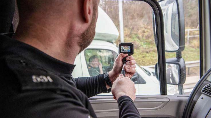 Police officer sitting in cab points a camera at a passing lorry