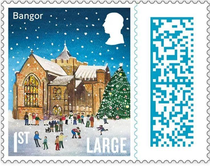 An illustrated version of St Deiniol's Cathedral in Bangor on a 1st class stamp. There is a large decorated christmas tree in the snow outside the building. children are playing and running. A family is with their dog and another group are building a snowman.