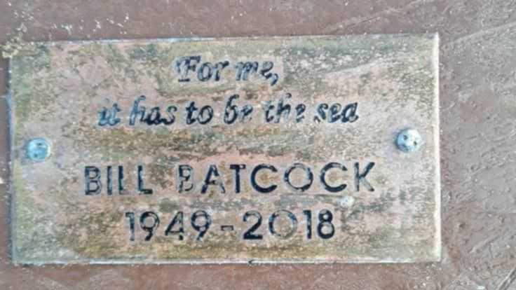 A weathered metal plaque nailed into a piece of wood bearing the words: "For me, it has to be the sea," above the inscription: "Bill Batcock - 1949 - 2018."