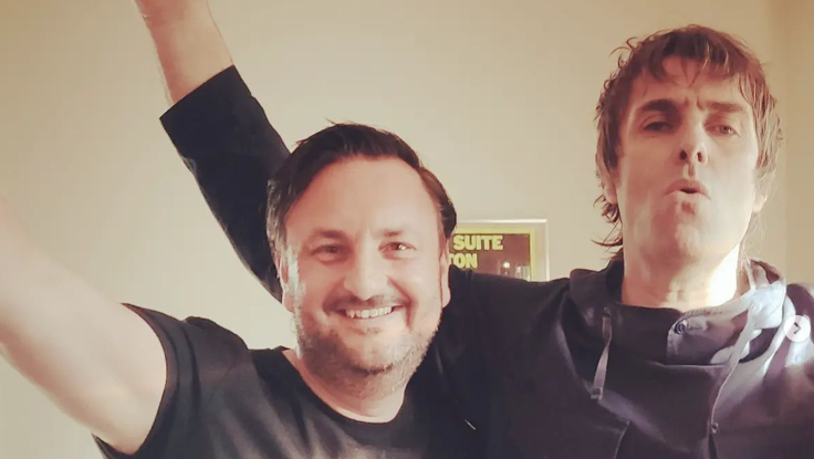 Nick Brine and Liam Gallagher both with their hands in the air. Liam is wearing a black hoodie, Nick a black t-shirt.