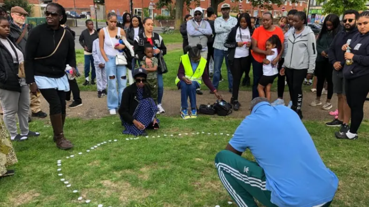 Mourners gathered around a circle of pebbles laid out on the grass