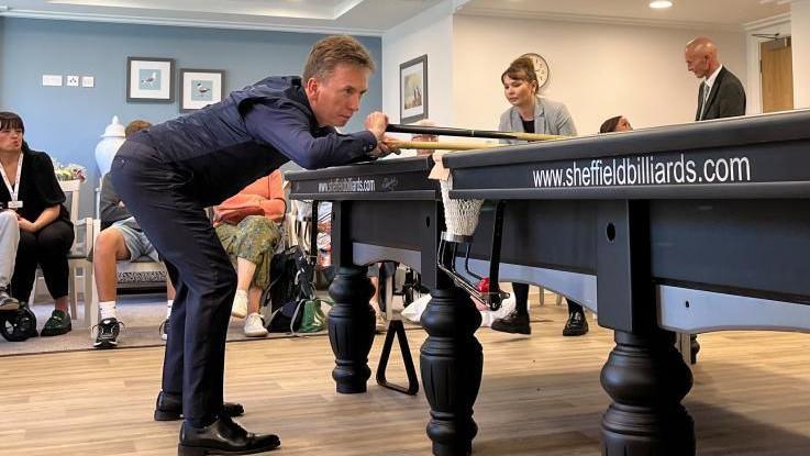 Ken Doherty leaning over a snooker table, with a cue in hand. He is wearing a dark blue outfit. 