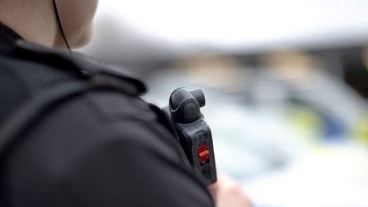 Over the shoulder shot of police officer in dark uniform with a small camera on chest.