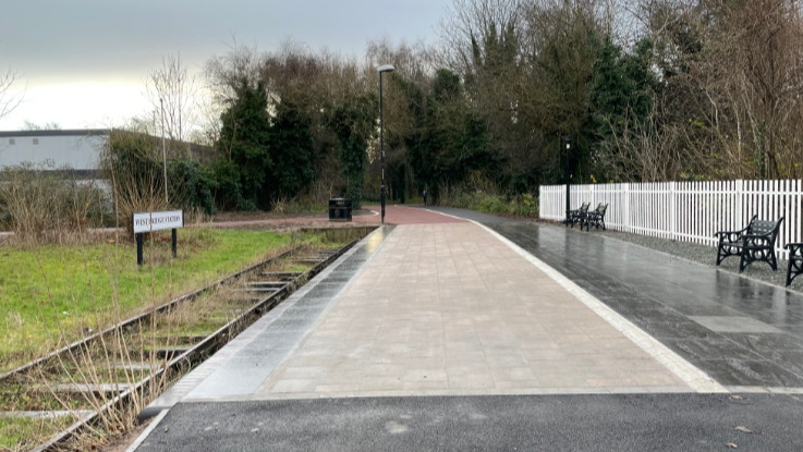 A railway platform next to a disused overgrown track. 
