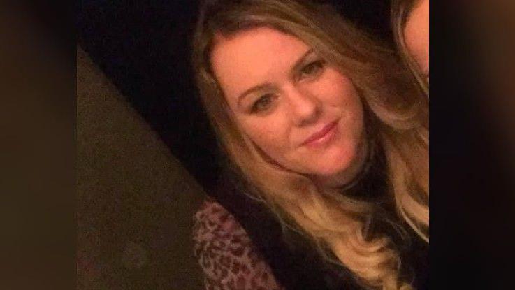 Kerry Rafferty smiling at the camera. She has long wavy blonde hair and is wearing a black top with leopard print sleeves.