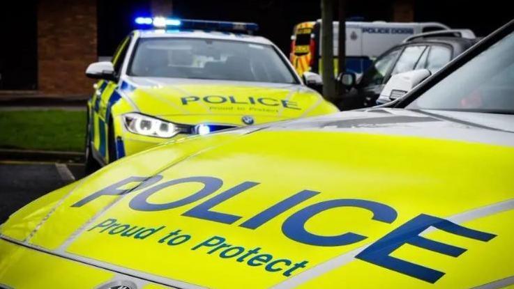 The bonnet of a Northumbria Police car emblazoned with "Police" "Proud to Protect" in the foreground. Behind it is the front of another, similar, police car