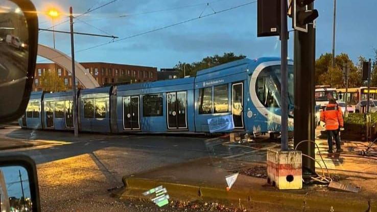 A crashed blue tram with an engineer in an orange coat standing near to a lamp post