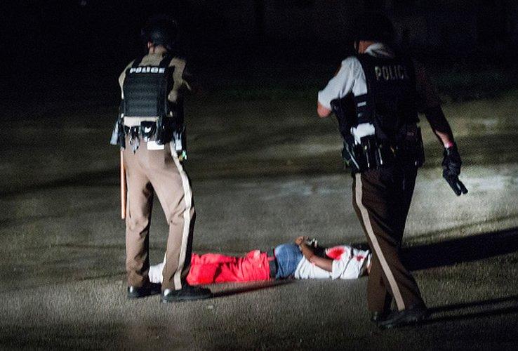 Police officers standing over handcuffed black suspect