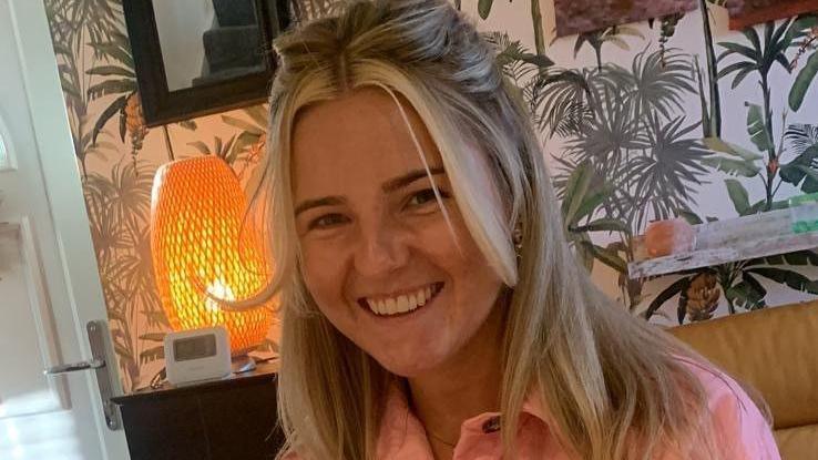 Summer smiles wearing a pink shirt in a living room decorated with a colourful wall paper.