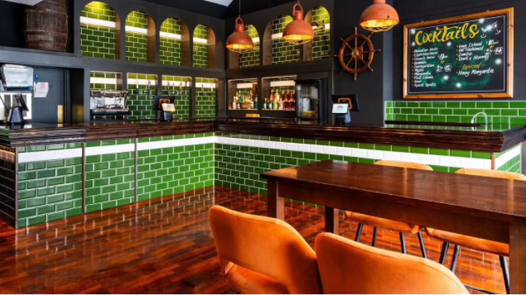 The inside of the bar with green tiling and a shiny floor - and a sign describing many cocktails 