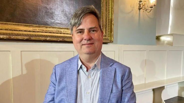 James Sandbach in a blue suit and shirt, sitting down