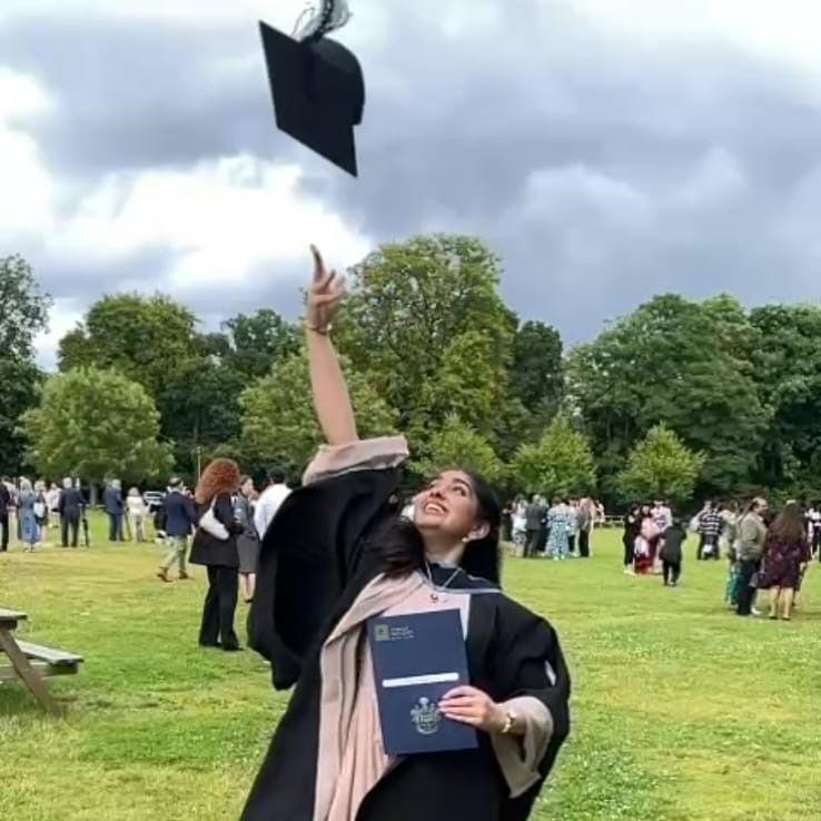 Miss Ahmed at her university graduation wearing her gown. She is smiling and throwing her cap into the air.