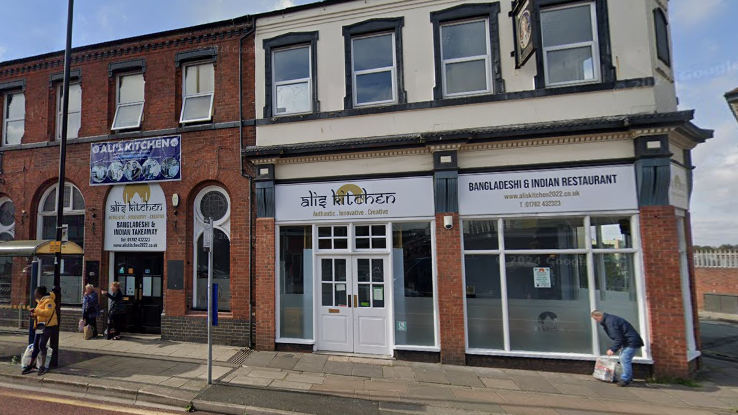 A view of a takeaway called Ali's Kitchen on a street with a bus stop. The restaurant has a white door and signage.