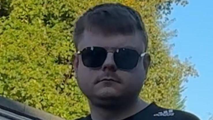 A man in his 20s with short brown hair wearing aviator sunglasses