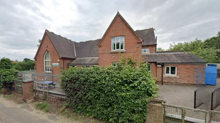 The exterior of Woodton Primary School, which is a two-storey red brick building with a playground.